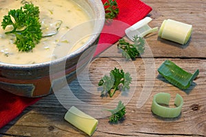 Cream sauce in a bowl with fresh leeks and herbs on rustic wood