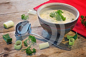 Cream sauce in a bowl with leek and herbs on rustic wood