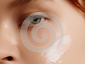 Cream smear. Beauty close up portrait of young woman with a healthy skin is applying a facial skincare product