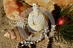 Cream snowman decoration on beach sand rock backdrop shell natural african beads red ball Christmas in July