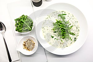 Cream soup with arugula and pine nuts in a white bowl