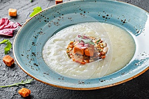 Cream soup of celery with tartare from baked vegetables decorated from croutons and arugula in plate on dark stone background
