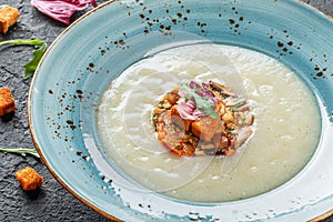 Cream soup of celery with tartare from baked vegetables decorated from croutons and arugula in plate on dark stone background