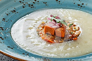 Cream soup of celery with tartare from baked vegetables decorated from croutons and arugula in plate on dark stone background
