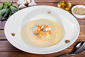 Cream soup with chicken breast, mushrooms, herbs on plate on dark wooden background.