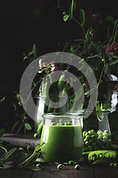 Cream soup from green peas in glass jar on brown wooden kitchen table background, vegan food concept, copy space, selective focus