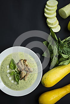 Cream soup of mashed potatoes with zucchini and basil and crackers on a dark background. Space for text