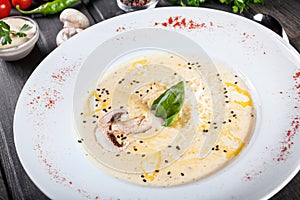 Cream soup with mushrooms, herbs, cheese parmesan, basil, sesame on plate on dark wooden background.