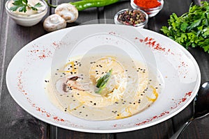 Cream soup with mushrooms, herbs, cheese parmesan, basil, sesame on plate on dark wooden background. Homemade food.