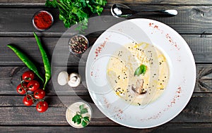 Cream soup with mushrooms, herbs, cheese parmesan, basil, sesame on plate on dark wooden background.