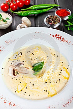 Cream soup with mushrooms, herbs, cheese parmesan, basil, sesame on plate on dark wooden background