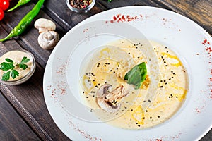 Cream soup with mushrooms, herbs, cheese parmesan, basil, sesame on plate on dark wooden background