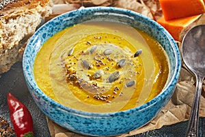 Cream-soup of orange color made of pumpkin, onion, pepper, potato and cauliflower in a blue plate decorated with pumpkin seeds and