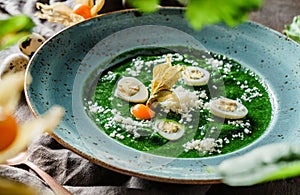 Cream soup with spinach, quail eggs and parmesan cheese in plate on wooden background. Healthy vegan food, clean eating, dieting,