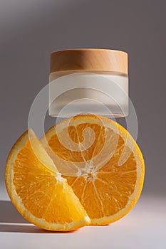 Cream with vitamin C in a frosted glass jar onto oranges. A container of a cosmetic product for skin care, makeup and