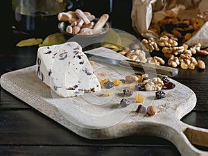 Creamery cheese with cranberries, nuts and raisins on wooden cutting board.