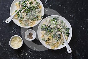 Creamy chicken, green peas, spinach farfalle pasta on a dark background, top view. Mediterranean style