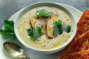 Creamy chicken soup with vegetables in bowl with chiabatta toast, parsley and nigela seeds sprinkle on stone table photo