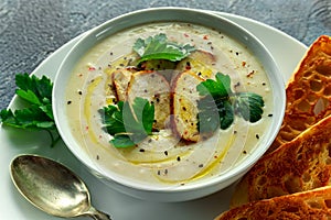 Creamy chicken soup with vegetables in bowl with chiabatta toast, parsley and nigela seeds sprinkle on stone table