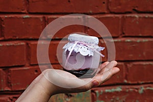 Creamy dessert in a small glass jar with decoration and ribbon which held in hand