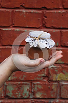 Creamy dessert in a small glass jar with decoration and ribbon which held in hand