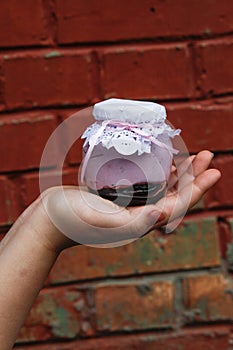 Creamy dessert in a small glass jar with decoration and ribbon which held in hand