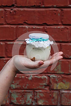 Creamy dessert in a small glass jar with decoration and ribbon which held in hand