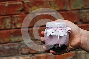 Creamy dessert in a small glass jar with decoration and ribbon which held in hand