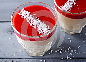 Creamy dessert with strawberry sauce and coconut flakes in glasses