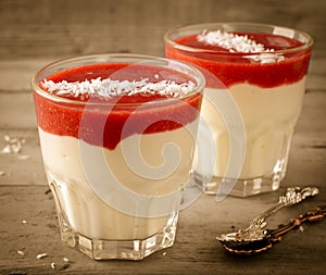 Creamy dessert with strawberry sauce and coconut flakes in glasses