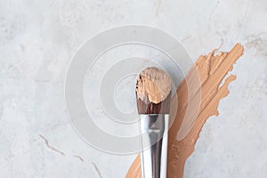 Creamy foundation smear and makeup brush on luxury marble background, above