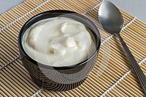 Creamy fruit yogurt in black bowl on reed table mat close up