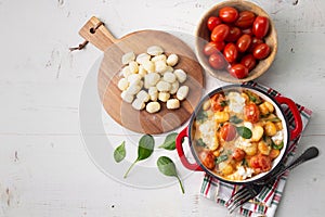 Creamy gnocchi with tomato sauce, spinach and mozzarella on a white wooden table