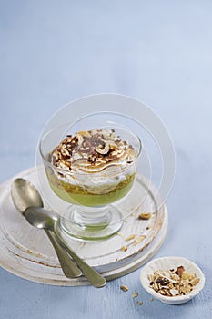 Creamy Green tea matcha dessert, mousse in a glass with hazelnut and burnt meringue on a light blue background with space for text