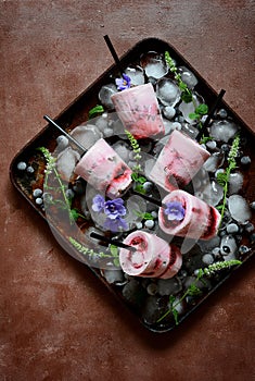 Creamy ice cream with berries of black currant, blueberry,raspberry, mint and flowers of violets on a dark background. Summer cool