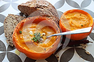 Creamy pumpkin soup and homemade bread on grey tiled table. Soup in a squash top view photo. Thanksgiving menu ideas.ÃÂ ÃÂ 