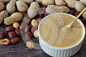 Creamy peanut butter in a bowl with golden spoon and roasted peanuts with shells on wooden table