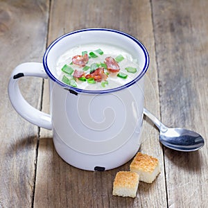 Creamy potato soup garnished with bacon and green onion, served in mug, square format