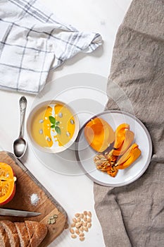 Creamy pumpkin soupwith pumpkin seeds and green, bread with bran and sliced pumpkin on wooden and fabric background. Top