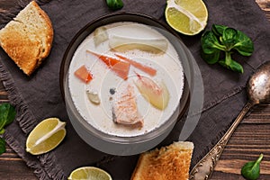 Creamy salmon soup with potatoes and carrots served with toast on a wooden rustic plank table. Finnish fish soup kalakeitto with