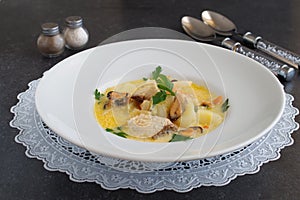 Creamy soup with fish fillet and mussels in a white plate on a white cloth on a grey abstract background. Healthy eating concept.