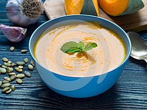 Creamy soup of pumpkin with mint on dark blue wooden background, garlic