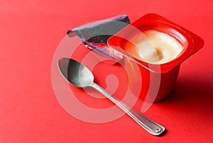 Creamy white vanilla opened yogurt plastic pot. Isolated on on red with selective focus and copy space