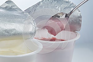 Creamy yogurt with cherry flavor in a spoon on the background of open plastic cups with yogurt of different flavors.