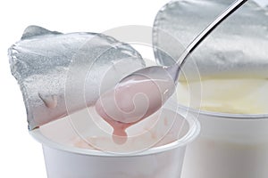 Creamy yogurt with strawberry flavor in a spoon on the background of open plastic cups with yogurt of different flavors.