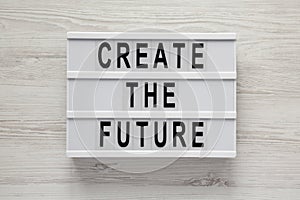`Create the future` word on lightbox on a white wooden background, top view. From above, flat lay, overhead