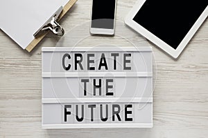 `Create the future` word on modern board, tablet, noticepad, smartphone on a white wooden background, top view. From above, flat