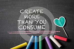 Create more than you consume. Text and colored pieces of chalk on a blackboard background photo