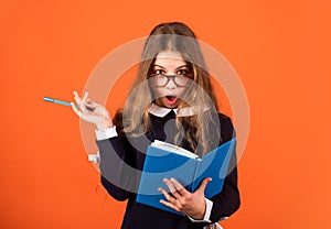 Create and surprise. Surprised schoolgirl with pen and book brown background. Little child keep mouth opened of surprise