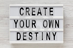 `Create your own destiny` words on a lightbox on a white wooden background, top view. Overhead, from above, flat lay. Close-up